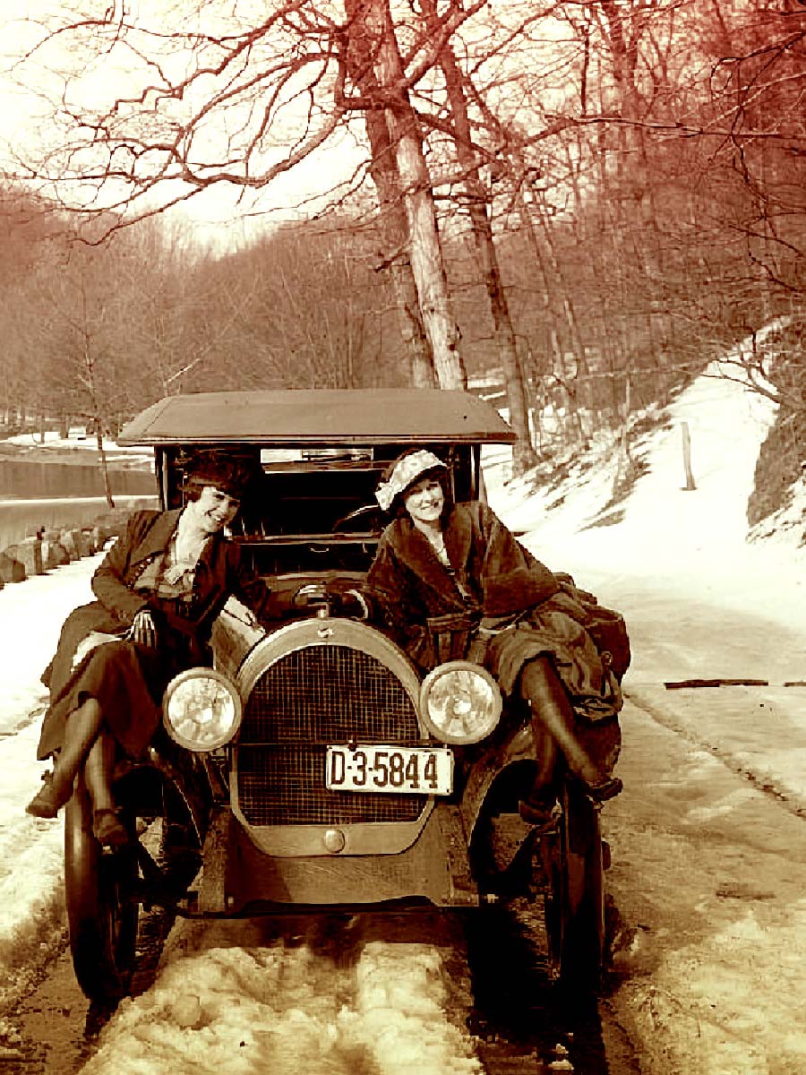 2 women pose on a 1920s car on a winter road