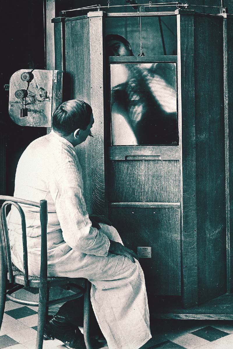 Early X-ray, doctor looks at man in x-ray cabinet